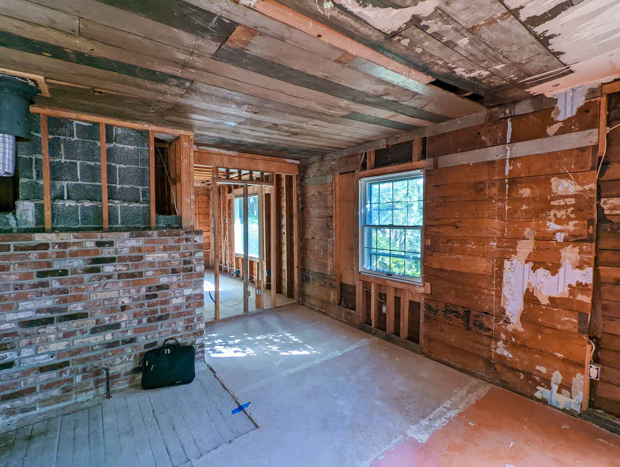 A room under renovation with exposed wooden studs and brickwork, unfinished ceiling and walls, a window letting in sunlight, and construction tools on the floor—capturing the process of home restoration in Seattle.