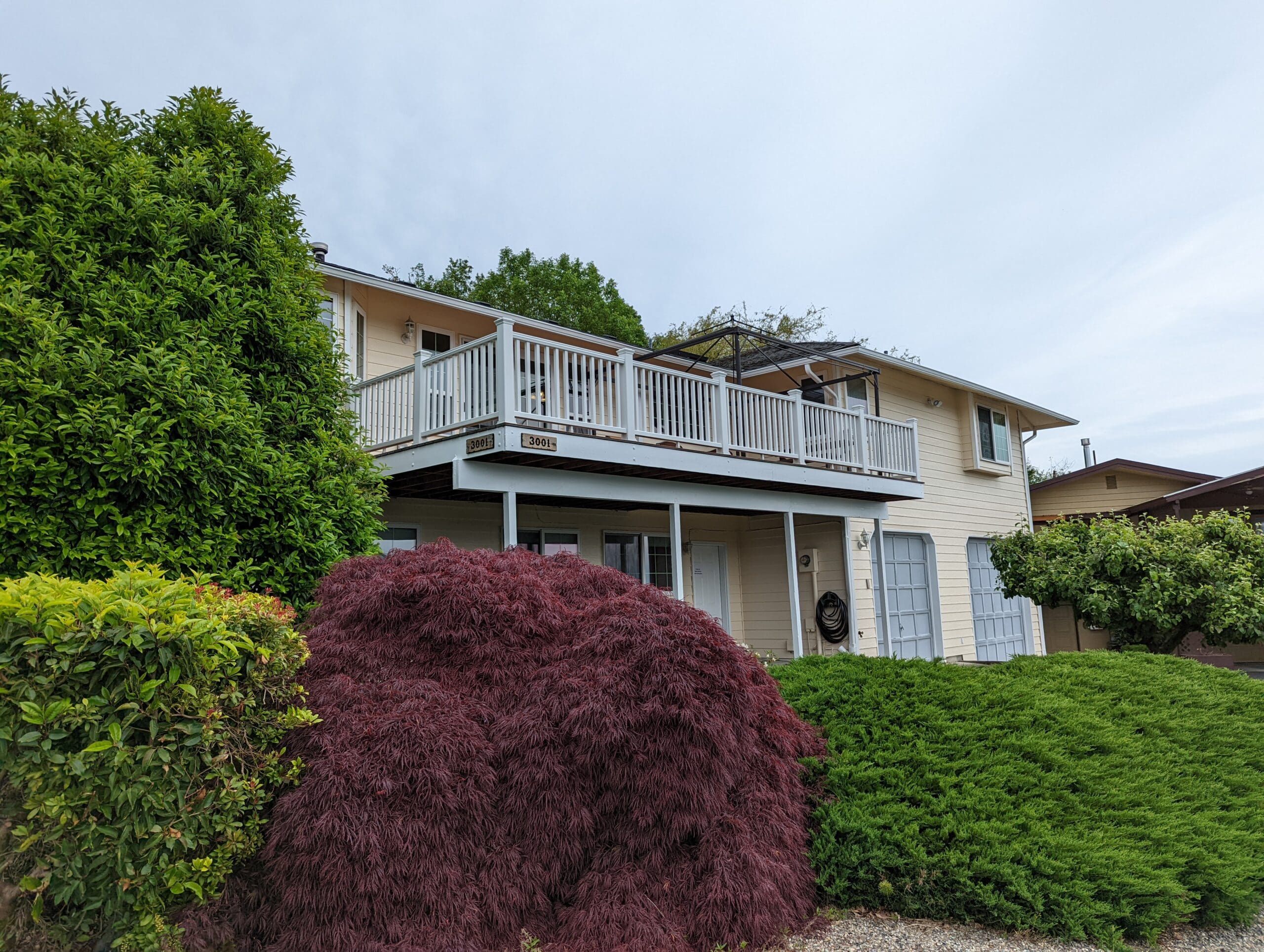 Freshly painted cream siding behind front deck and lush landscaping after exterior painting