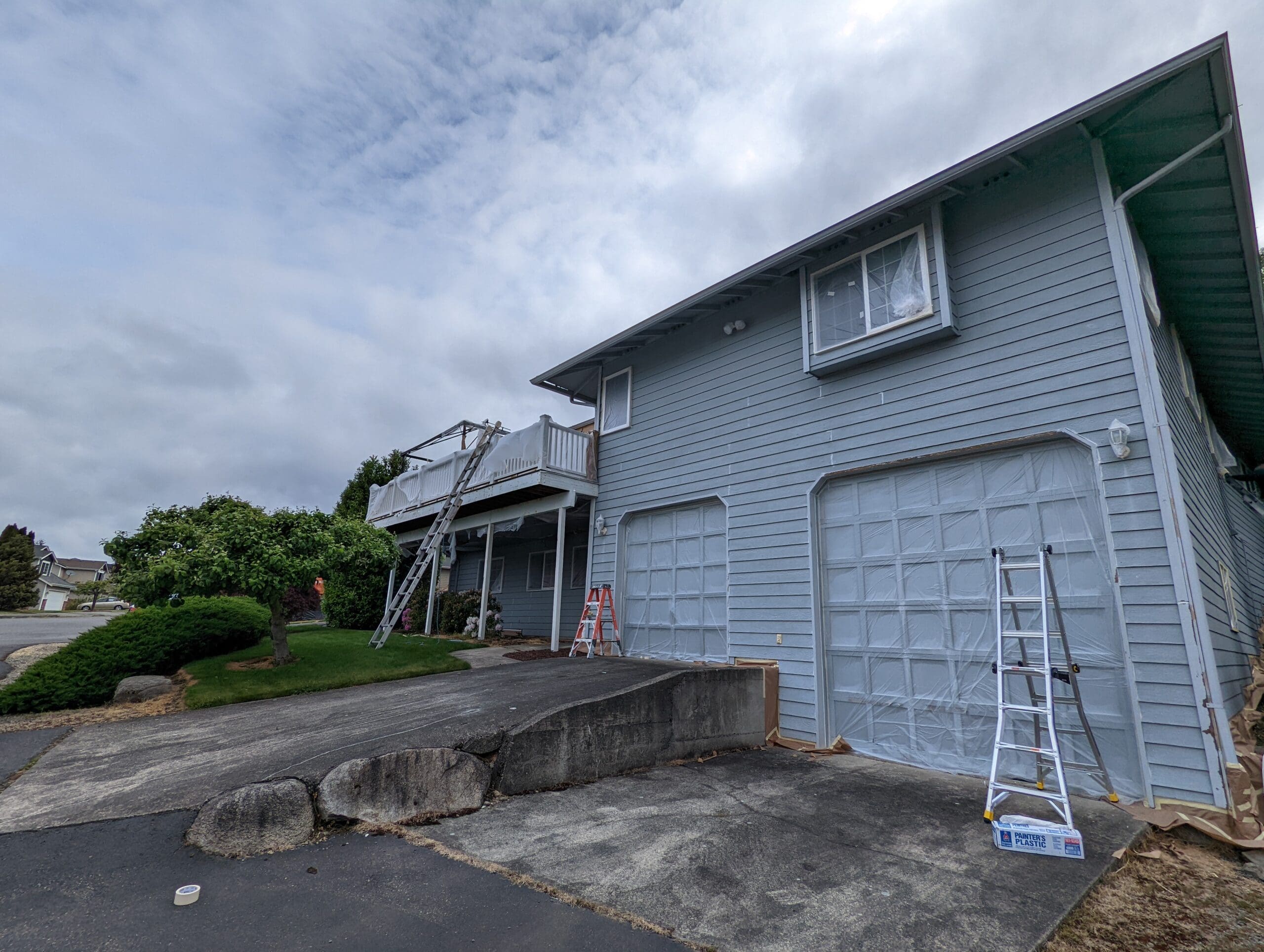 Garage doors and siding masked with plastic and paper before exterior repainting