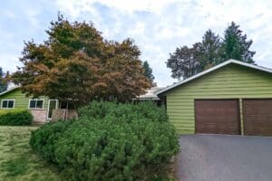 After exterior photo of green lap-siding home with white trim and brown double garage doors.