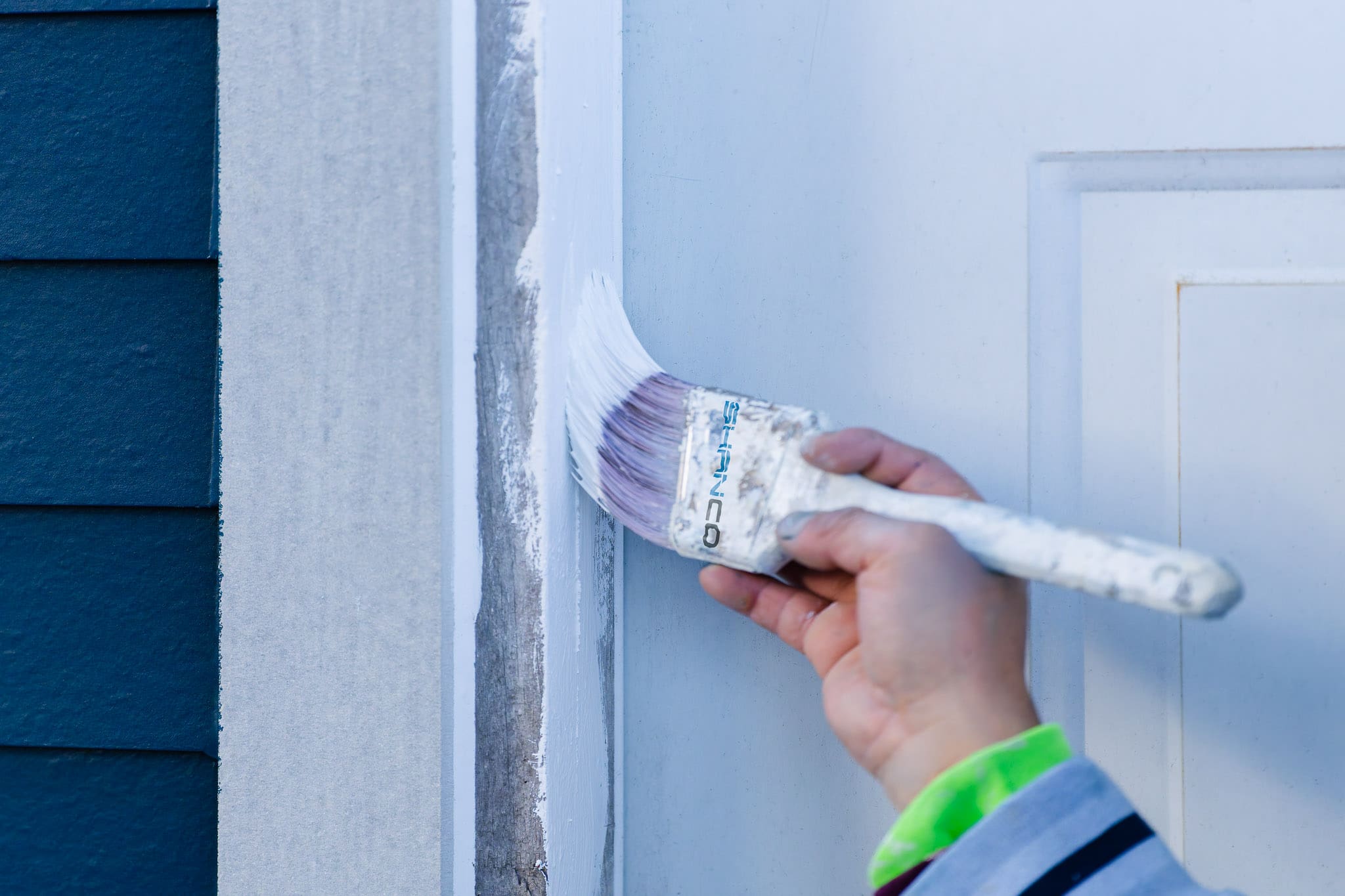 Shanco Painter applying white paint to exterior door trim next to blue siding in King County, Washington.